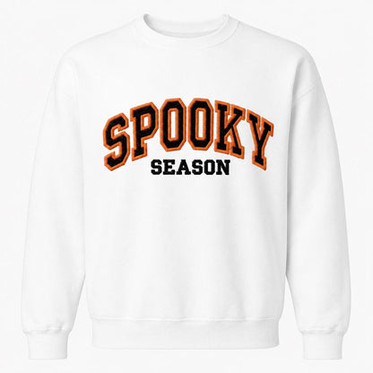 A white crewneck sweatshirt with "SPOOKY SEASON" embroidered across the chest in orange and black varsity-style letters.
