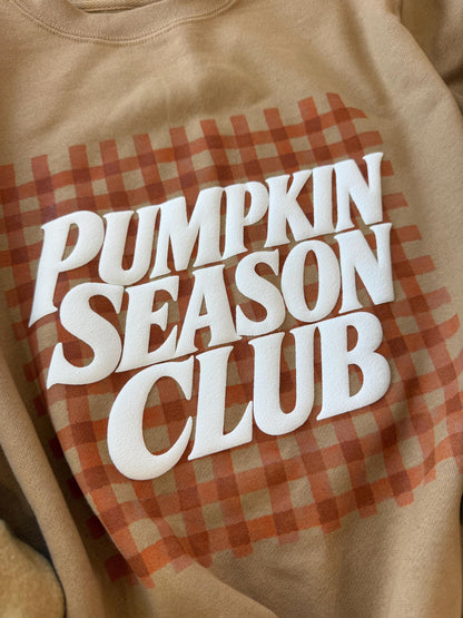 A close-up of a tan sweatshirt with "PUMPKIN SEASON CLUB" in white text over an orange gingham pattern.