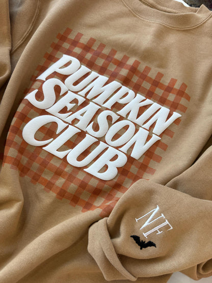 A tan sweatshirt with "PUMPKIN SEASON CLUB" in white text over an orange gingham pattern, and "NF" with a black bat embroidered on the left sleeve.