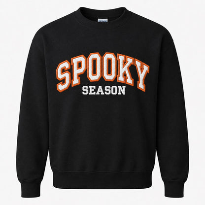 A black crewneck sweatshirt with "SPOOKY SEASON" embroidered across the chest in orange and white varsity-style letters.